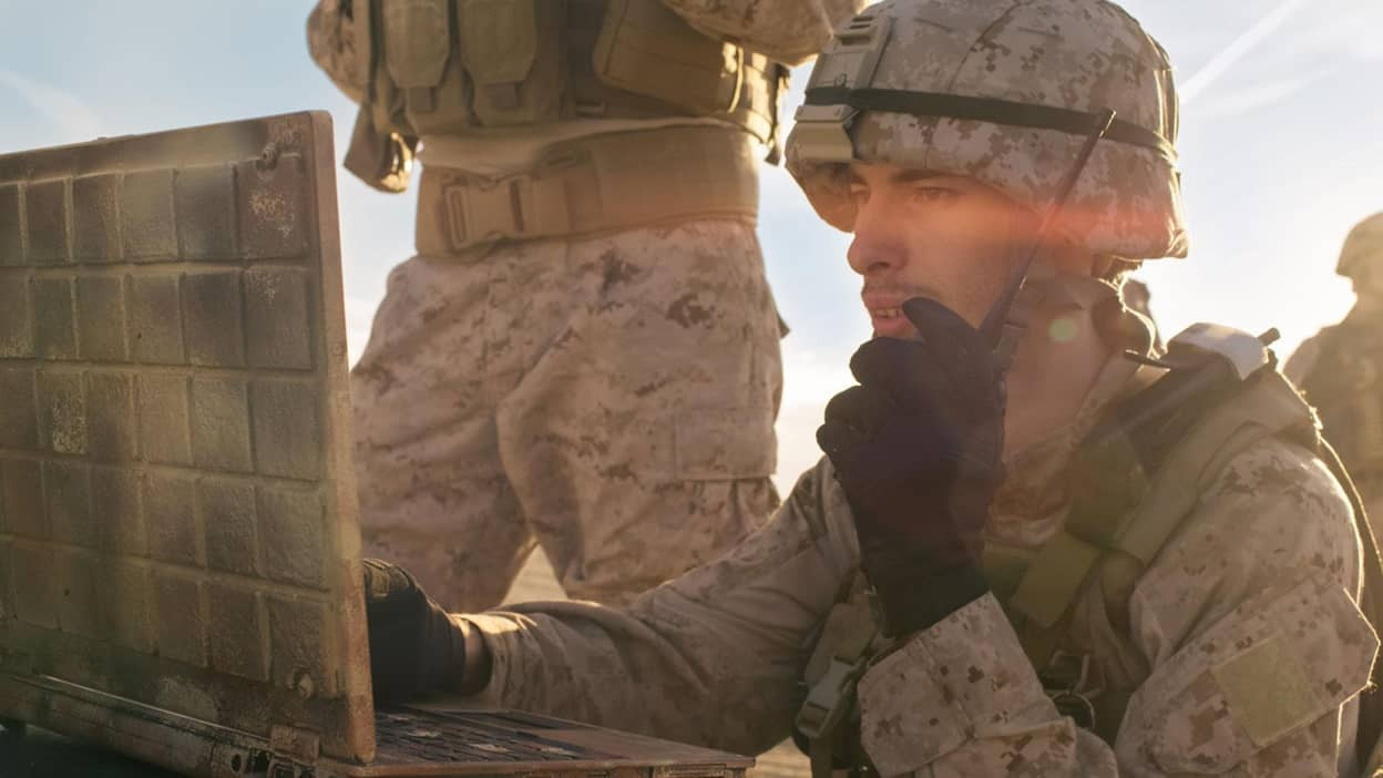 military personnel using a laptop on the battlefield